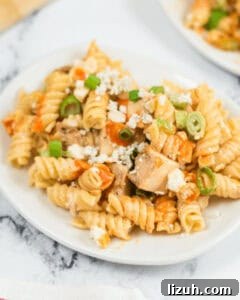 A plate of rotini chicken pasta salad mixed with diced chicken, crumbled blue cheese, and sliced green onions.