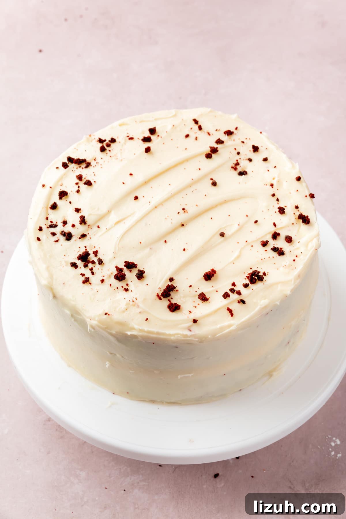 Gluten-Free Red Velvet Cake Recipe: Moist, Rich & Simple to Make 13 A red velvet cake frosted with cream cheese frosting and sprinkled with red velvet cake crumbs on top of a white cake stand.