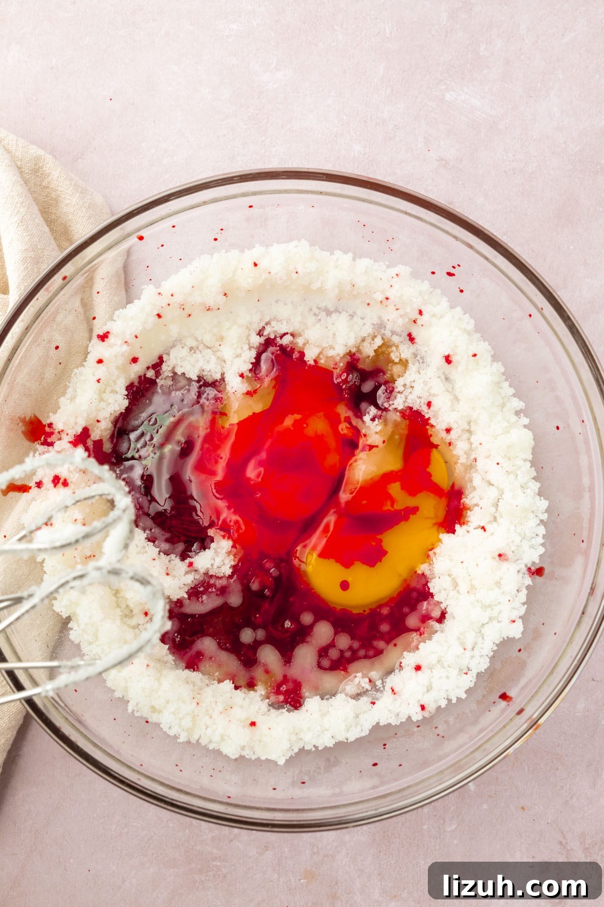 Gluten-Free Red Velvet Cake Recipe: Moist, Rich & Simple to Make 7 A bowl of granulated sugar, red food dye, vanilla, and eggs with two beaters.