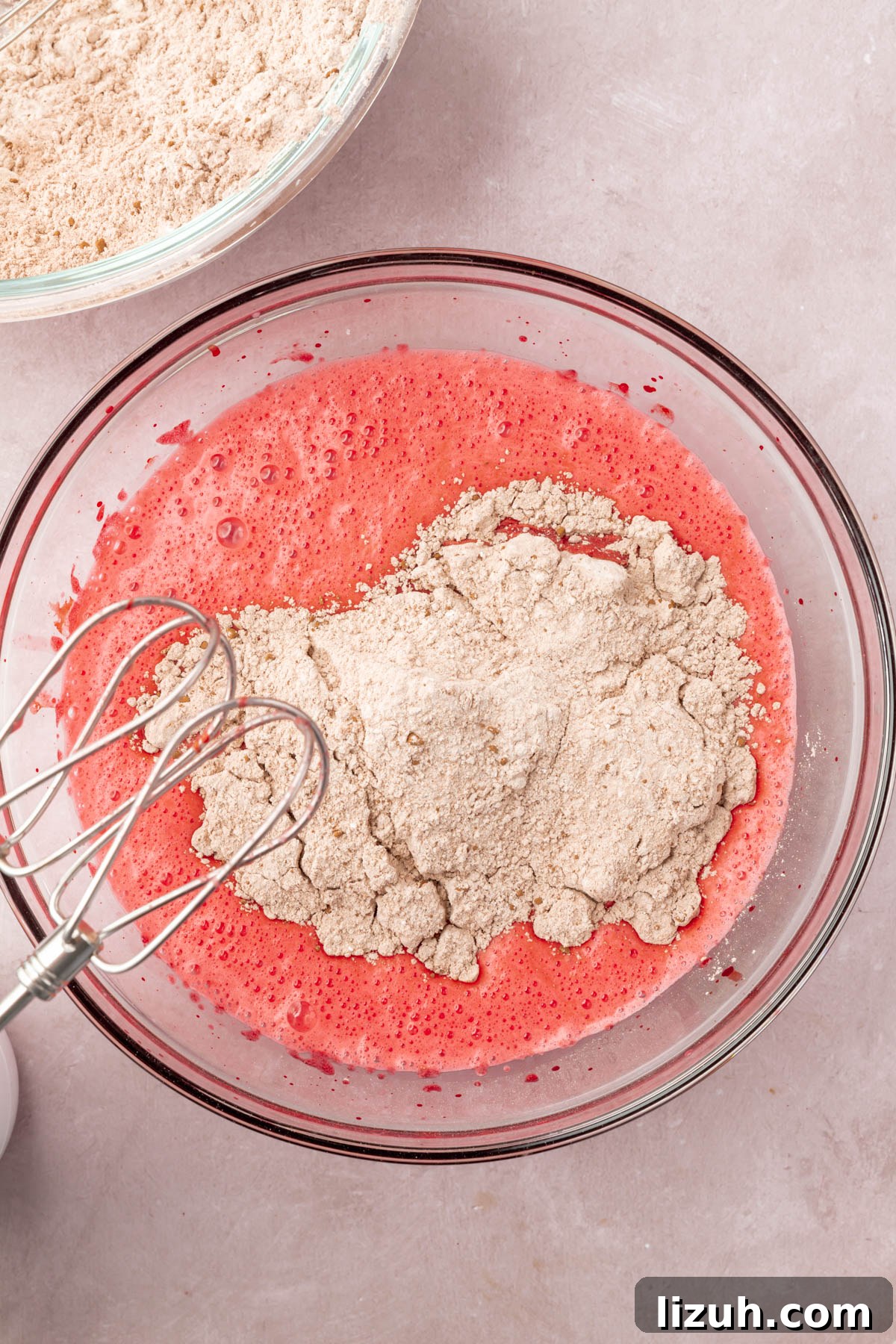 Gluten-Free Red Velvet Cake Recipe: Moist, Rich & Simple to Make 9 Red cake batter with brown dry ingredients in a glass mixing bowl with two whisk beaters.