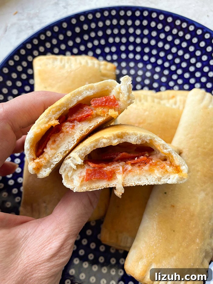 Three homemade pizza pockets on a dark blue Polish pottery plate with white polka dots and another hot pocket cut in half held above the three pizza pockets.