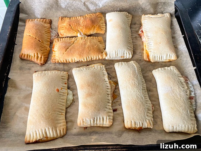 Pizza hot pockets sitting on a baking sheet lined with parchment paper.