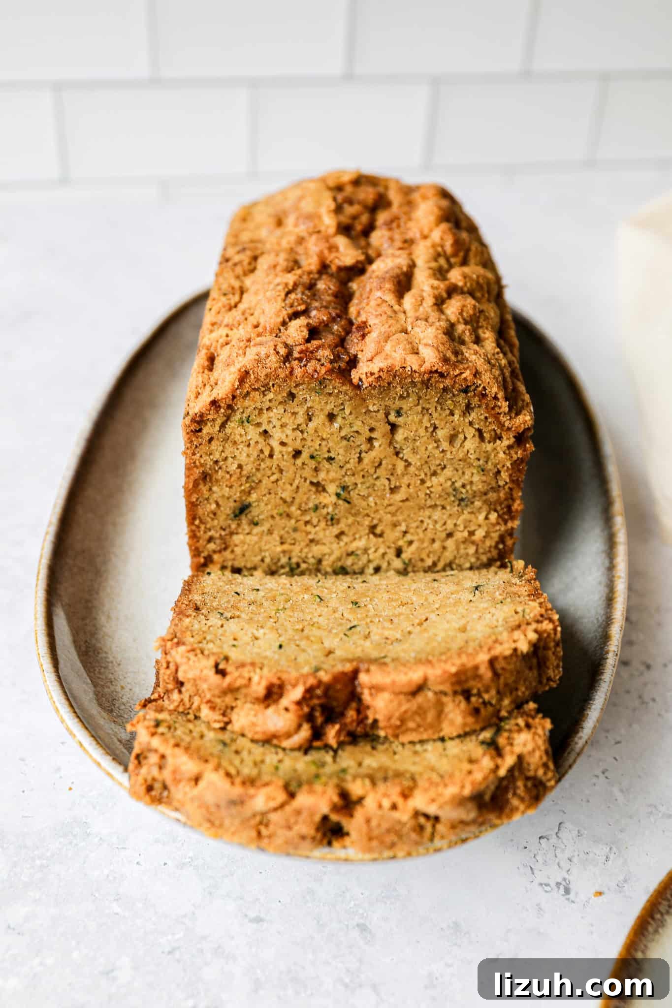 an oval serving plate with a loaf of gluten free zucchini bread on it with two slices cut and laying in front of the bread loaf