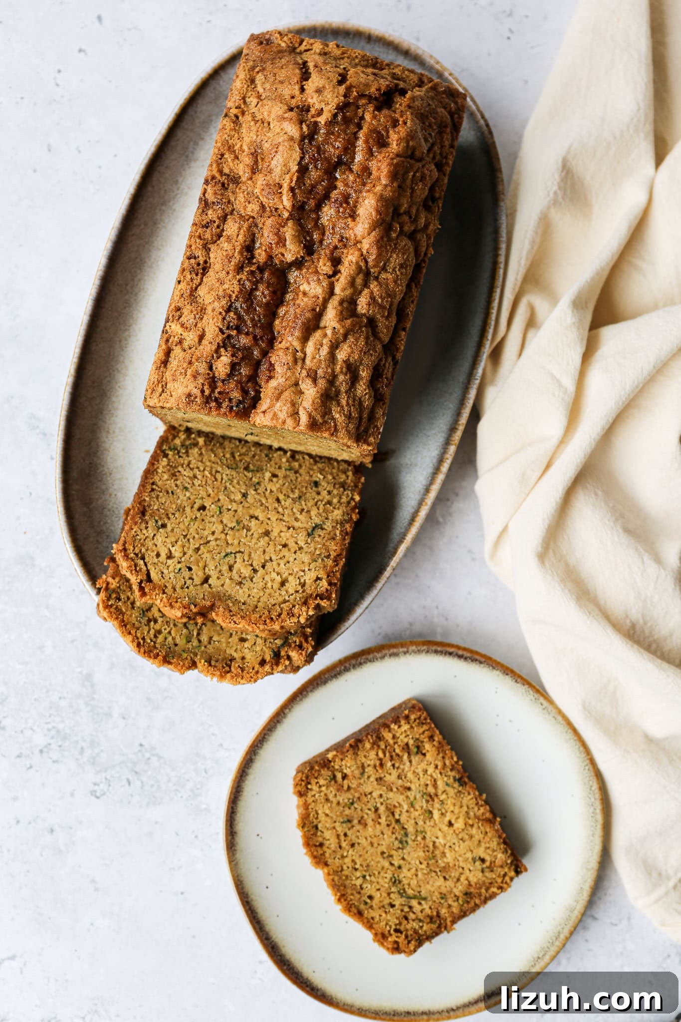a loaf of gluten free zucchini bread on an oval plate with two slices cut from the loaf laying in front of it and one slice on a plate beside the oval plate