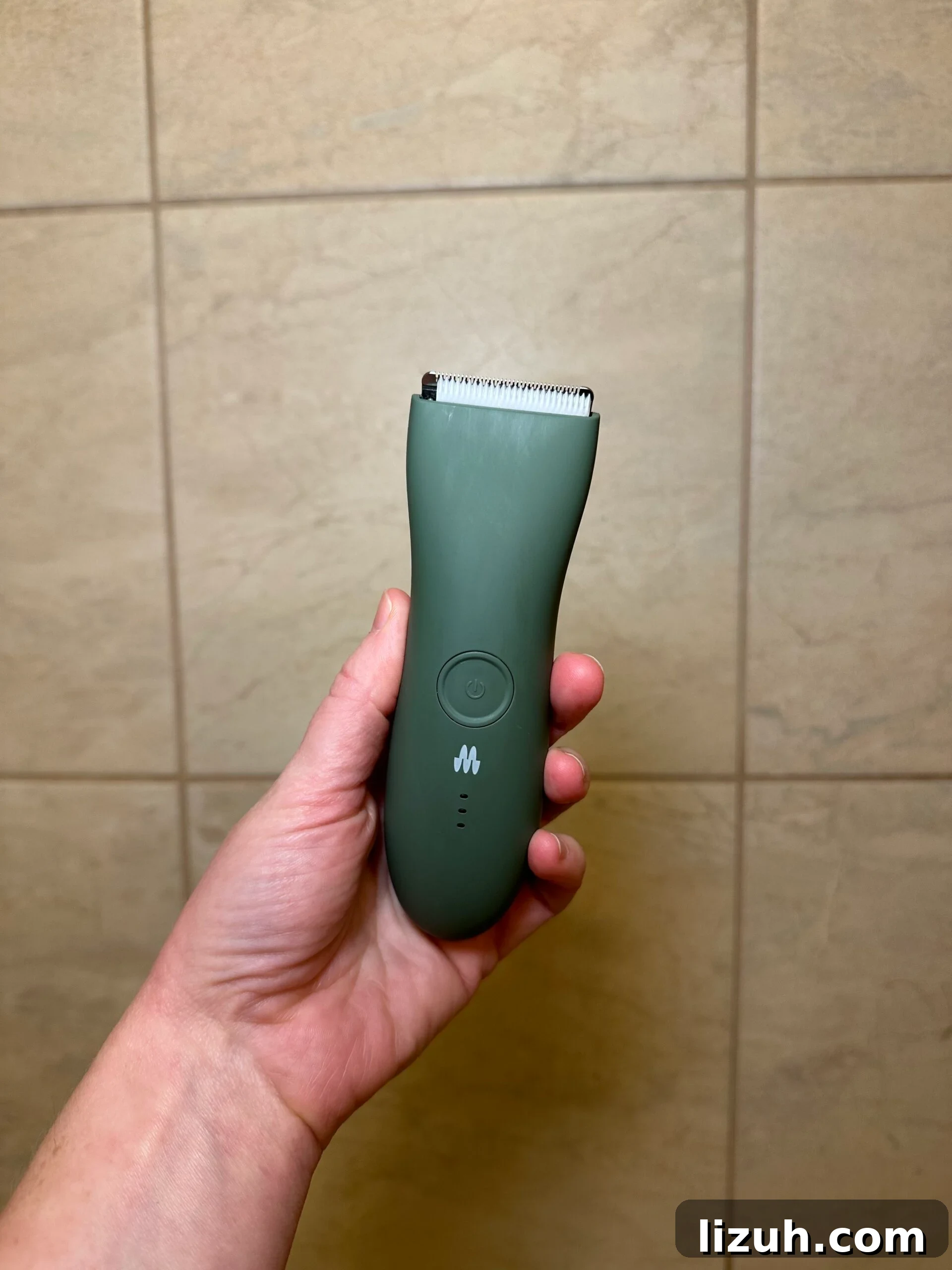 PFAS-Free, Non-Toxic Razors Reviewed: What to Buy in 2026 5 Hand holding a green Meridian body hair trimmer in front of beige tiled wall.