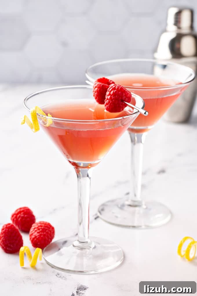 Two martini glasses with a martini garnished with fresh raspberries and a lemon twist.