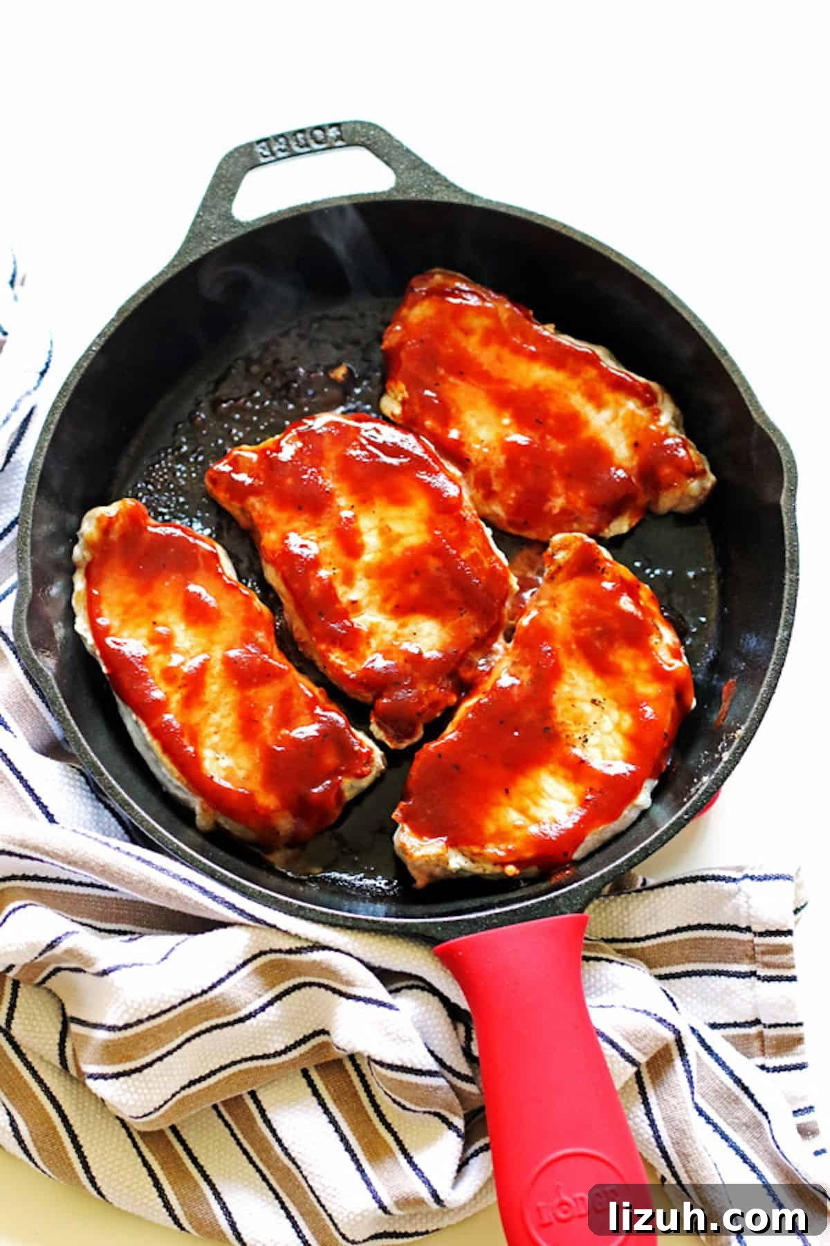 A cast iron pan with four cooked bbq pork chops in it.