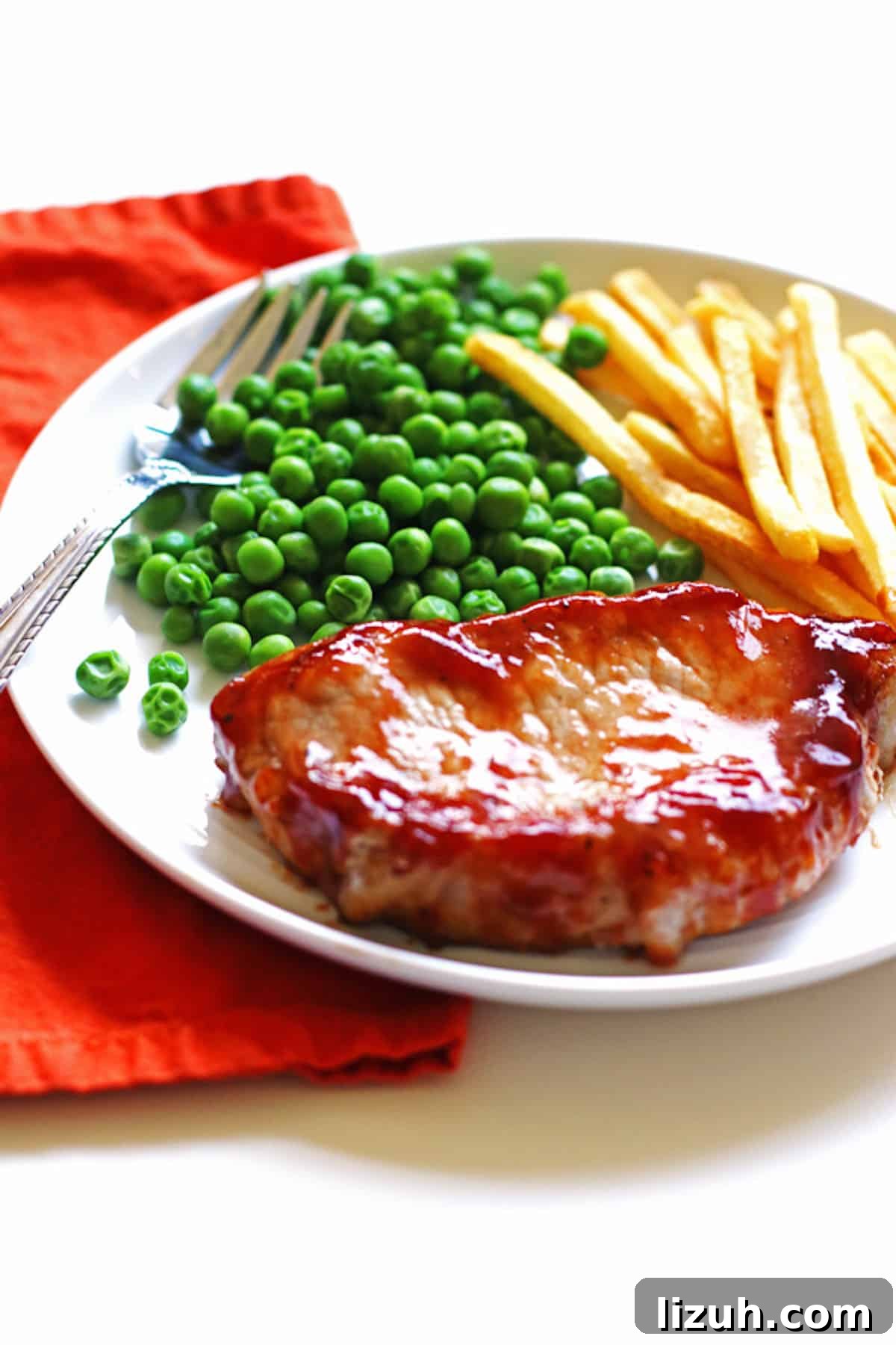 A white plate with a barbecue pork chop, peas, and french fries.