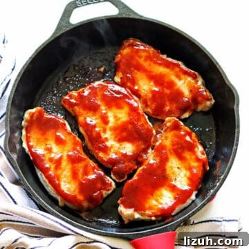 A cast iron pan with four cooked bbq pork chops in it.