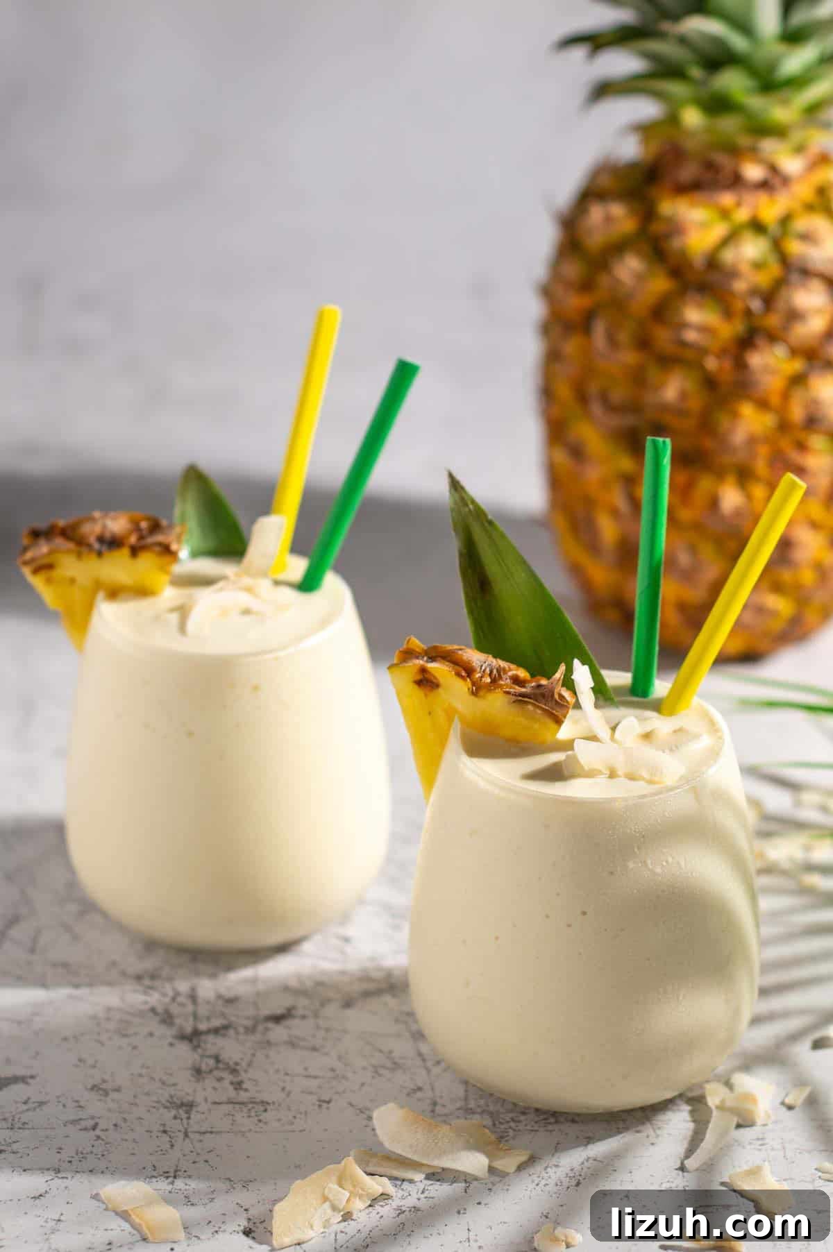 Ultra-Creamy Piña Colada Smoothie — No Banana, No Ice 2 Two pina colada smoothies with a pineapple in the background.