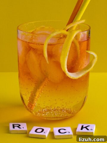 A medium glass of Rock shandy on a yellow background with an orange and yellow straw.
