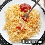 frozen shredded hash brown potatoes cooked in the air fryer and topped with ketchup on a white plate