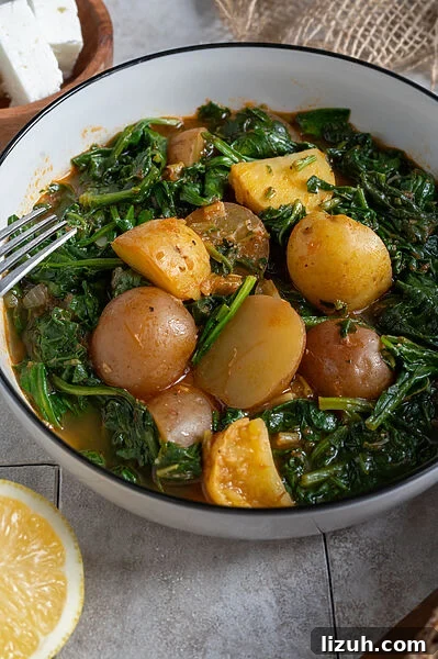 Greek Potato Yahni: Classic Mediterranean Potato Stew Recipe 9 Spinach and potato stew in a white bowl, surrounded by feta, olives and bread.