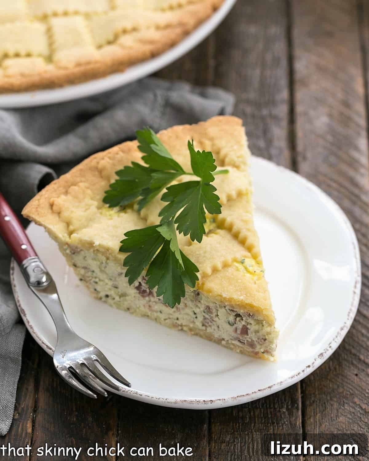 Italian Pizza Rrustica - a savory Italian pie fillled with ricotto, mozzarella and prosciutto Slice of pizza rustica on a white plate with a parsley sprig on top.