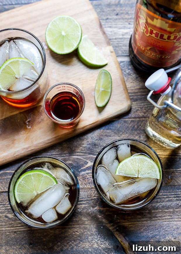 Pumpkin Spice Dark and Stormy Cocktail Recipe 6 Cocktails on a wooden surface surrounded by a cutting board, slices of lime, ginger beer and Kahlúa Pumpkin Spice.