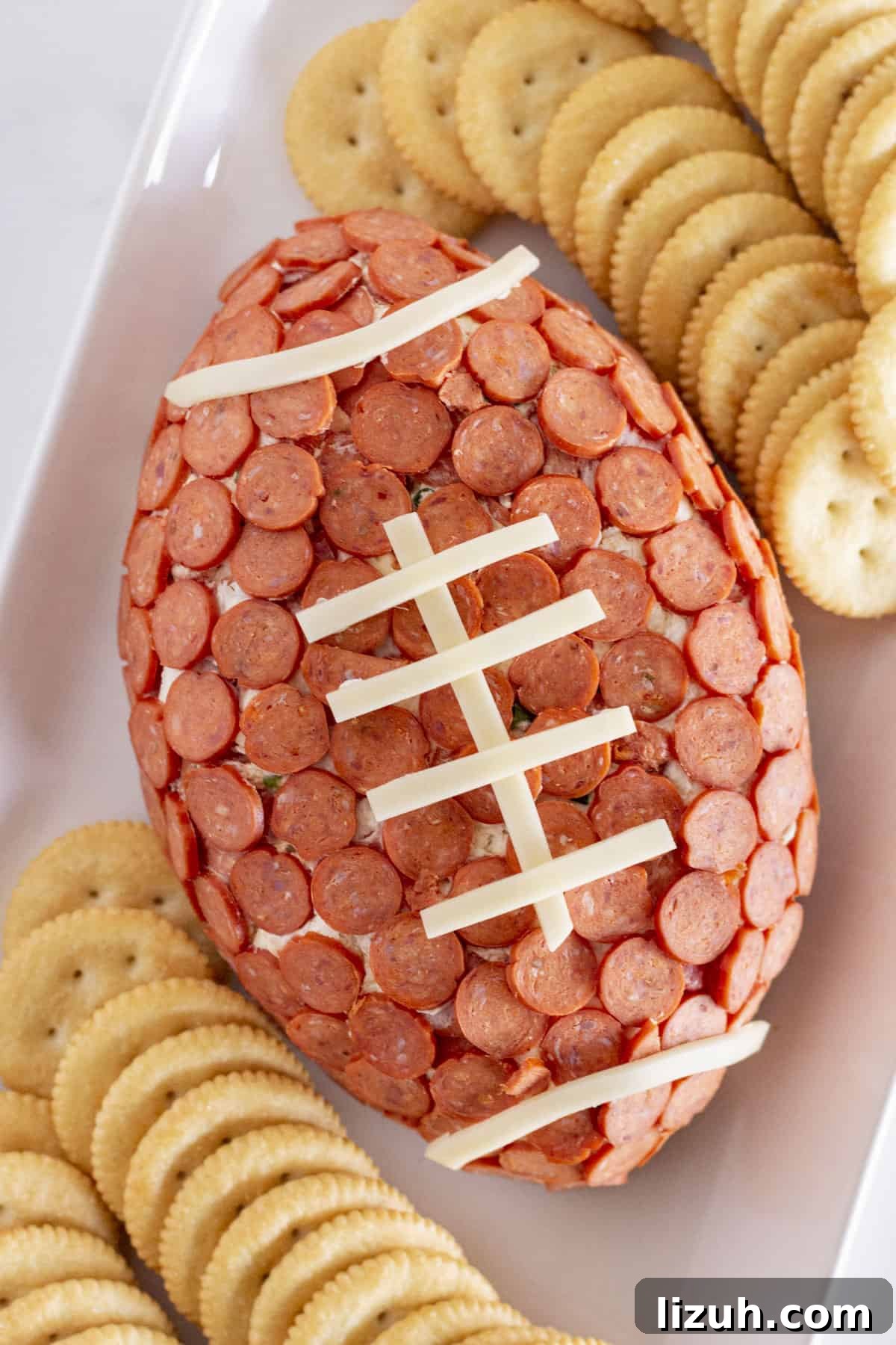 Pepperoni Pizza Cheese Ball Game-Day Appetizer 2 A football cheese ball on a white plate with crackers for serving.