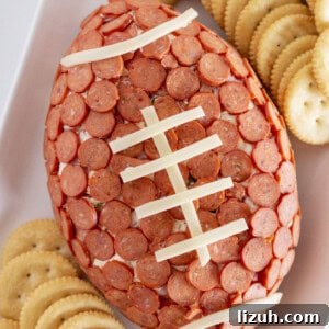 Pepperoni Pizza Cheese Ball Game-Day Appetizer 12 A football pepperoni cheese ball on a white tray with crackers.