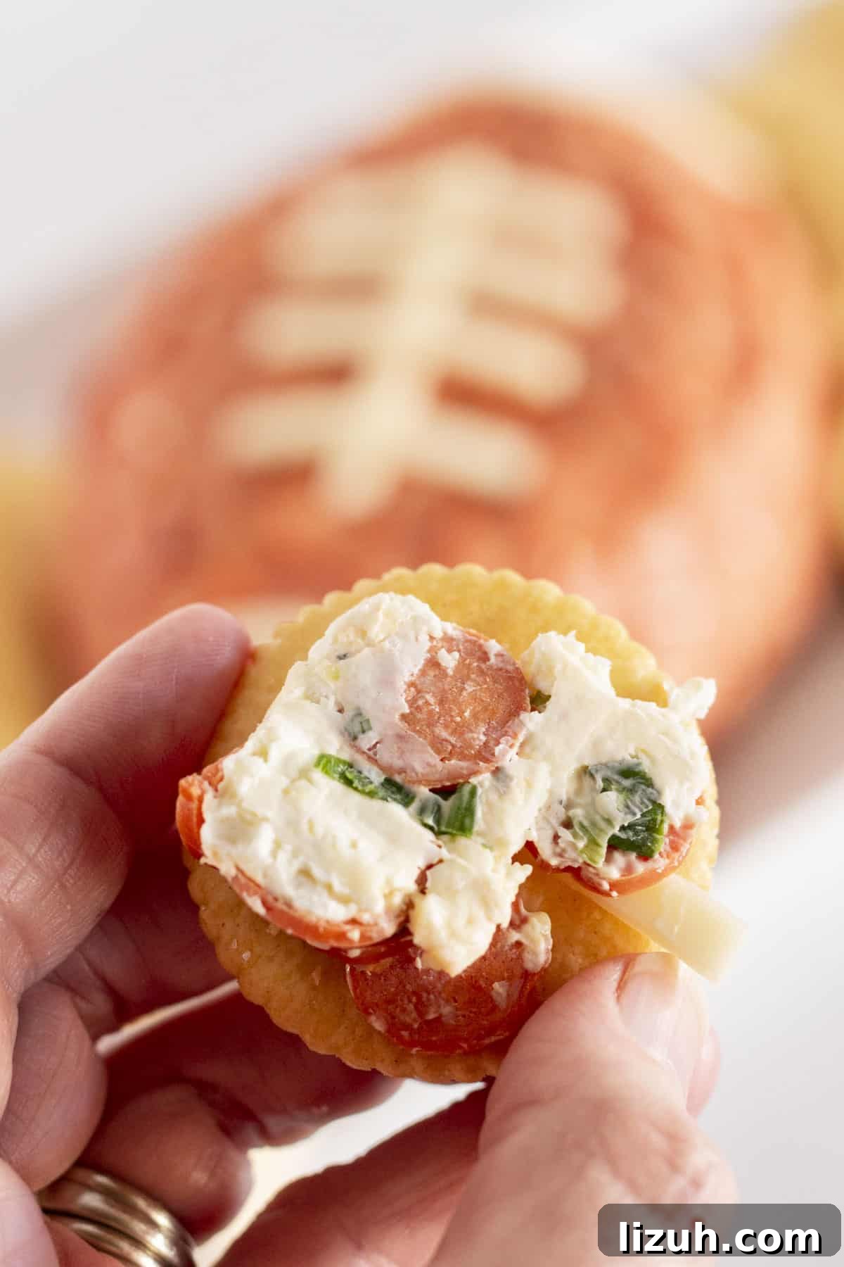 Pepperoni Pizza Cheese Ball Game-Day Appetizer 7 Serving the football cheese ball on a cracker.