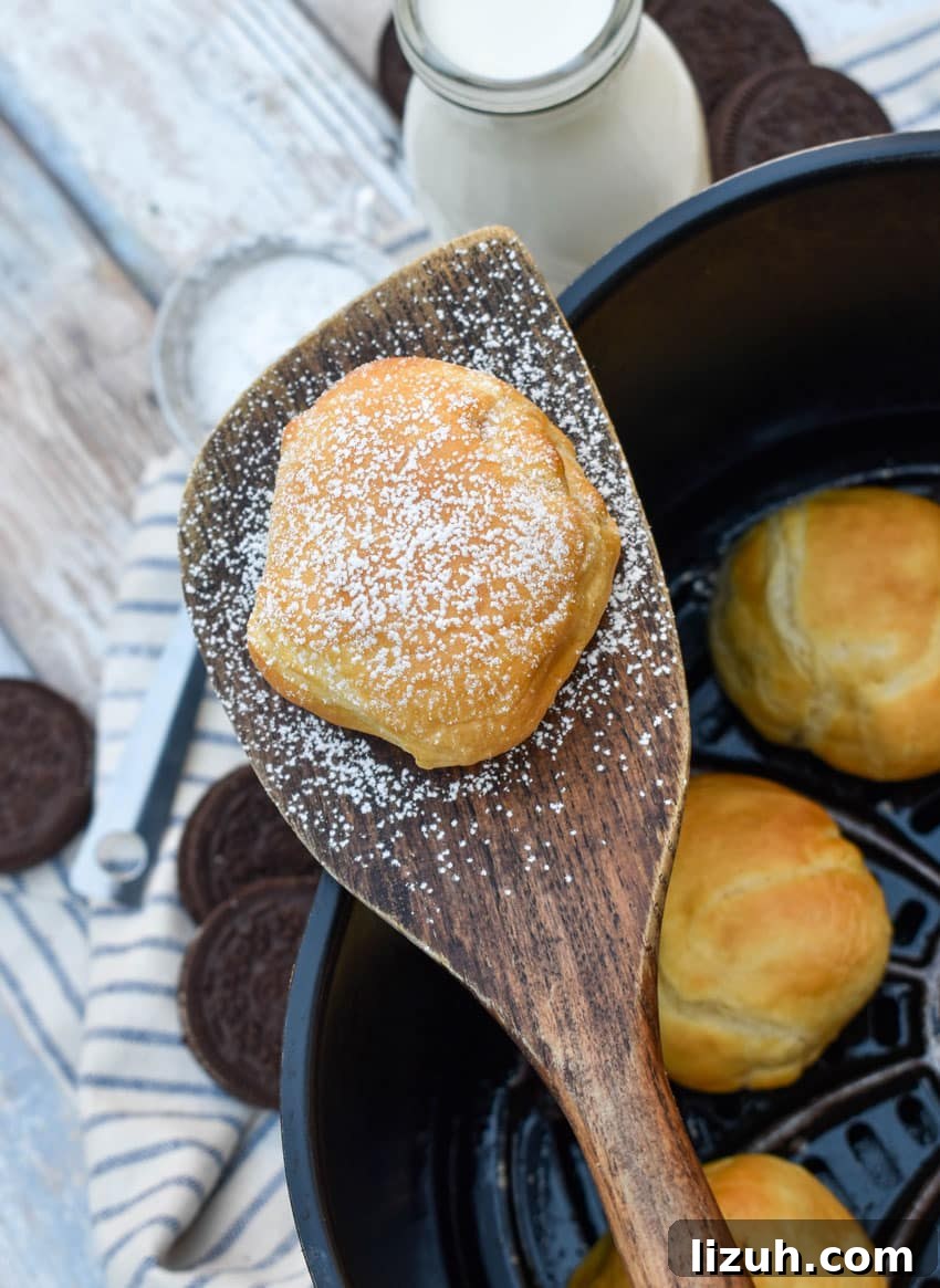 a wooden spatula holding up a powdered sugar dusted air fried oreo