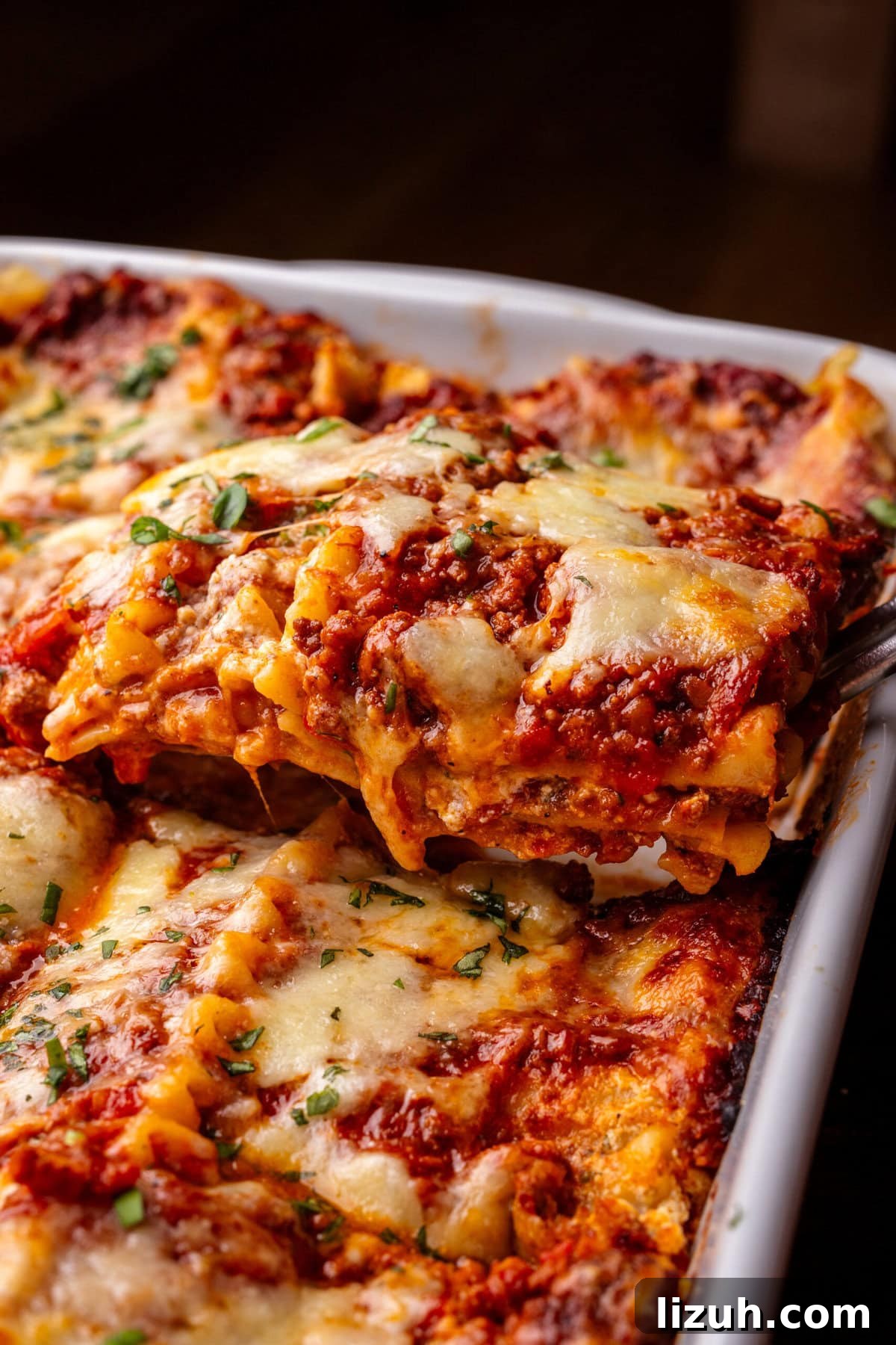 A slice of lasagna bolognese being lifted out of a white baking dish with a spatula.