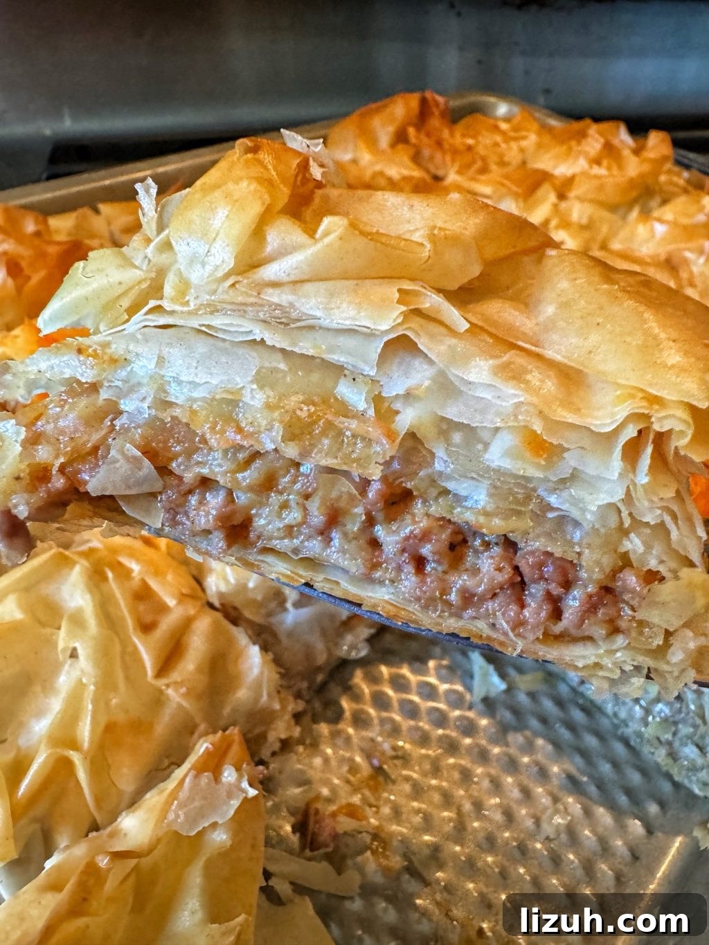 A close up of a slice of phyllo dough pastry with ground meat inside above a baking dish