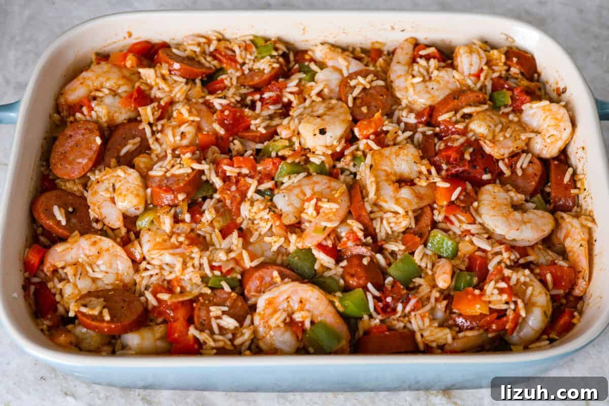 Overhead shot of shrimp sausage and veggies mixed with rice, tomatoes, and seasonings in a baking dish.