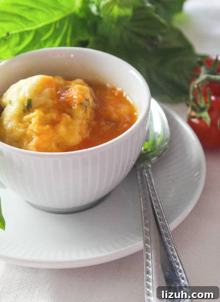 A bowl of tomato soup and cup of soup in a white cup garnished with fresh basil.