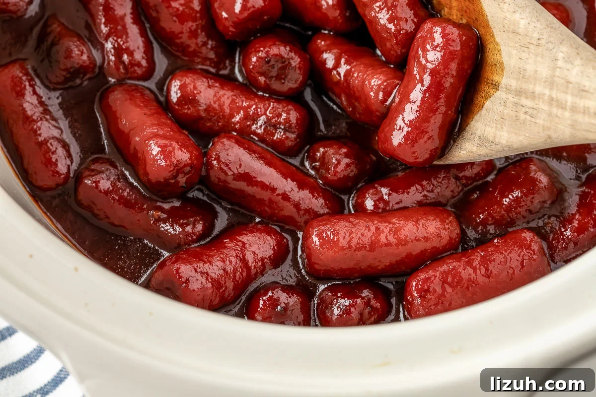 Slow Cooker Little Smokies Recipe: Sweet & Tangy Party Sausages 3 Little smokies simmering in a slow cooker with grape jelly and chili sauce.