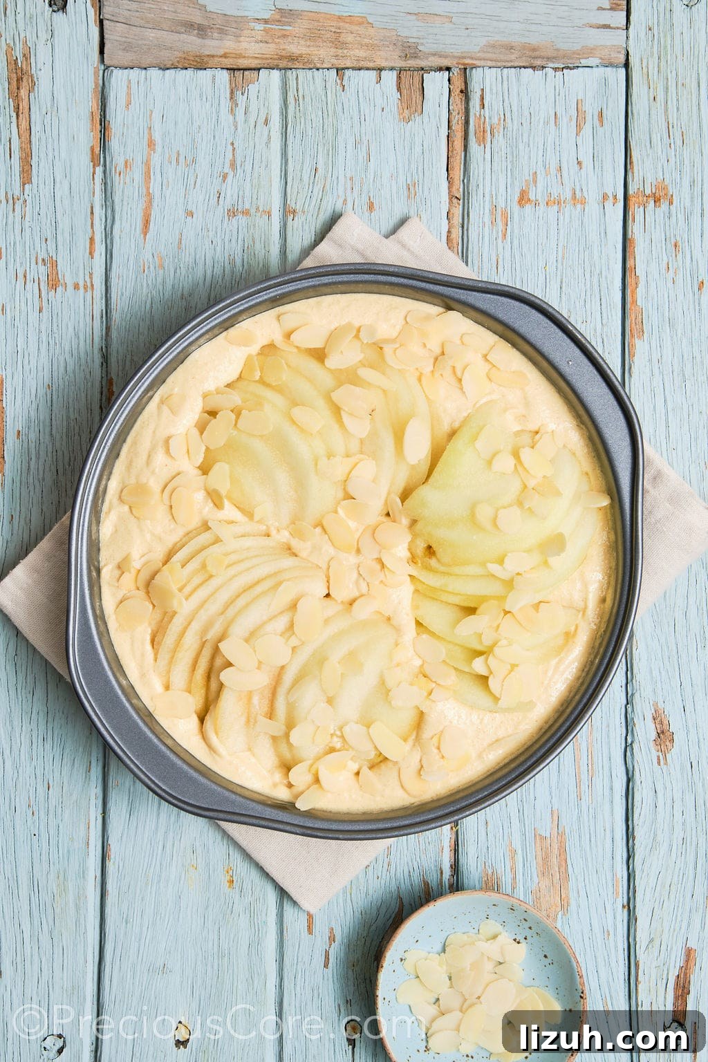 cake batter topped with sliced pears and almond flakes.
