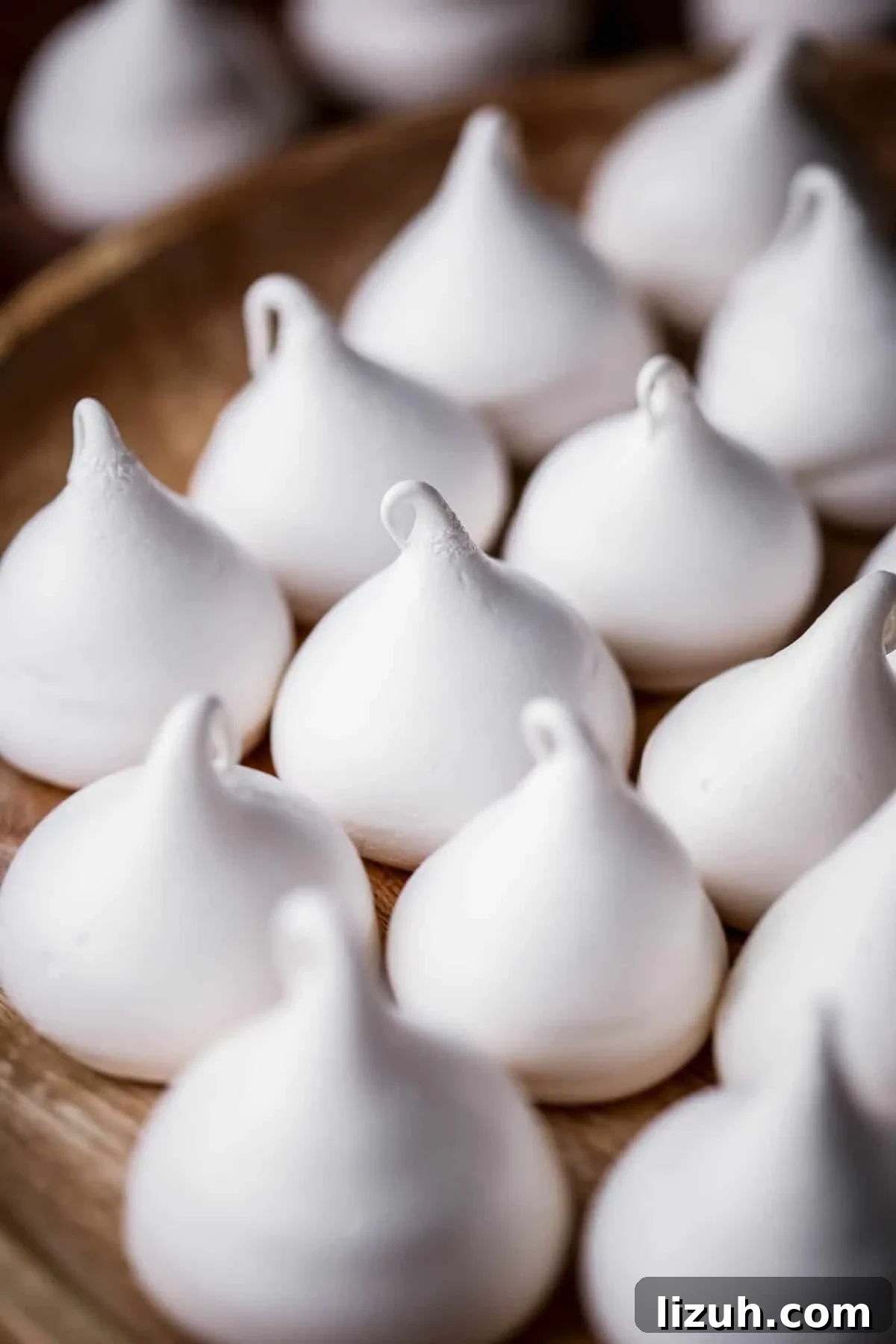 White Meringue Kisses on a wooden plate.