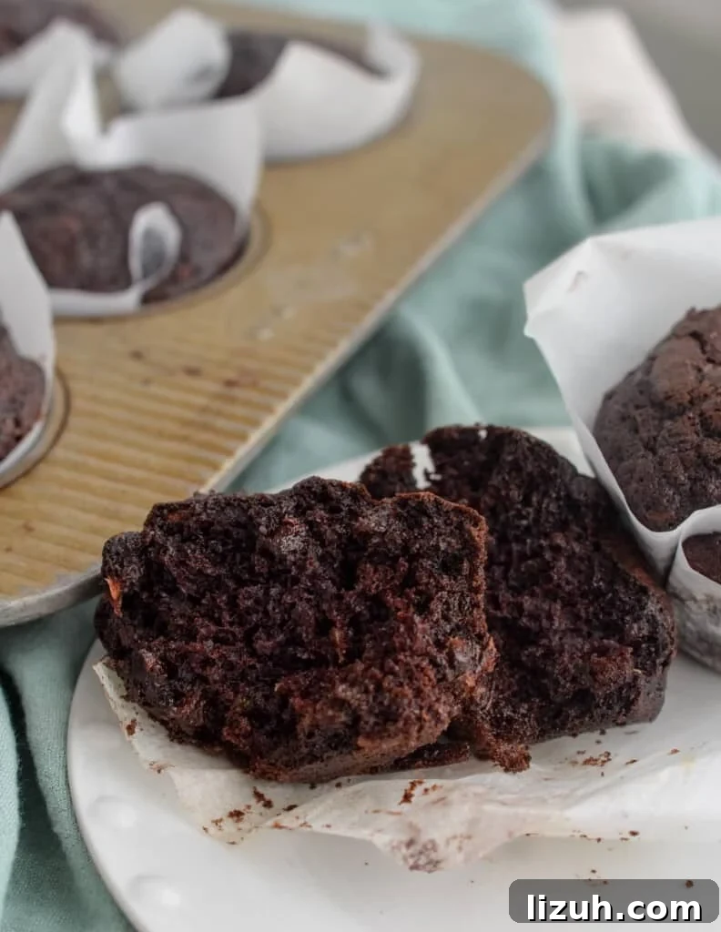 Chocolate zucchini muffin broken in half on a piece of parchment paper.