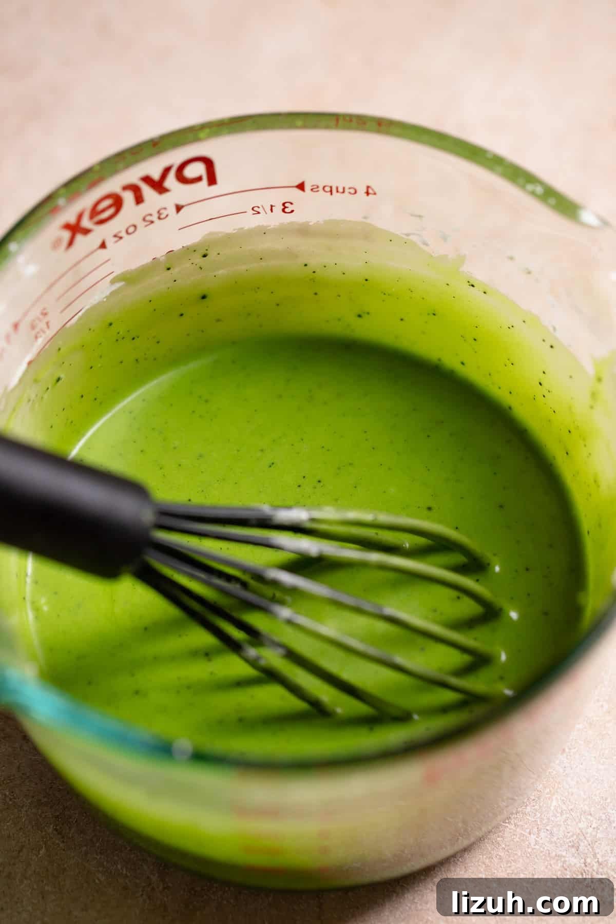 Matcha icing in a glass bowl with a whisk.