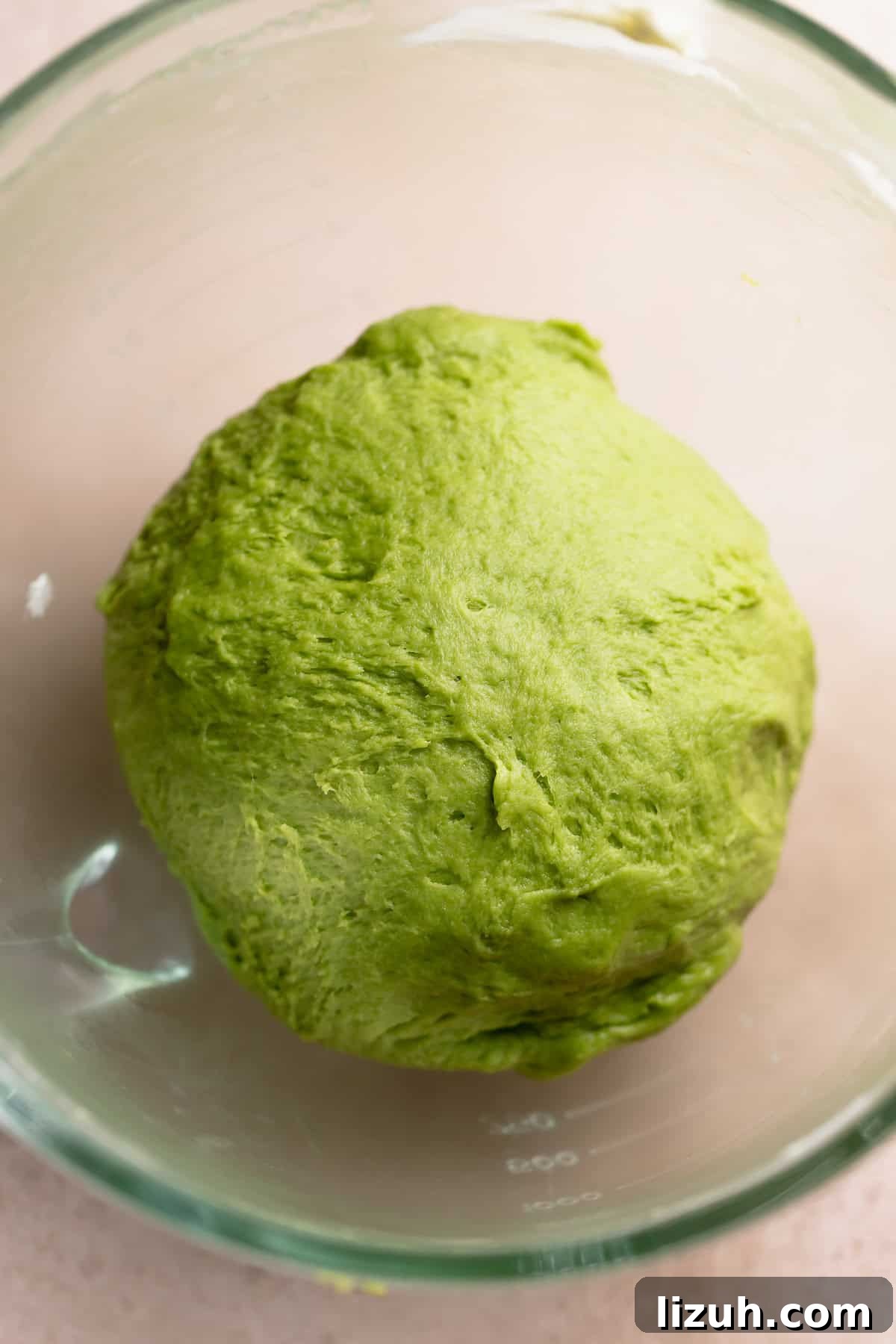 Matcha dough ball in a glass mixing bowl resting.