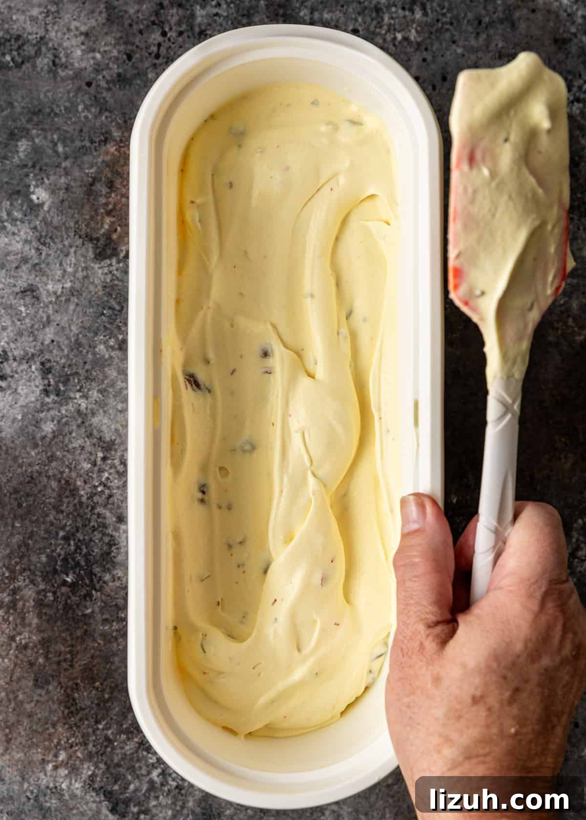 overhead: a hand holding a spatula to smooth out the bastani sonnati ice cream in an insulated ice cream tub