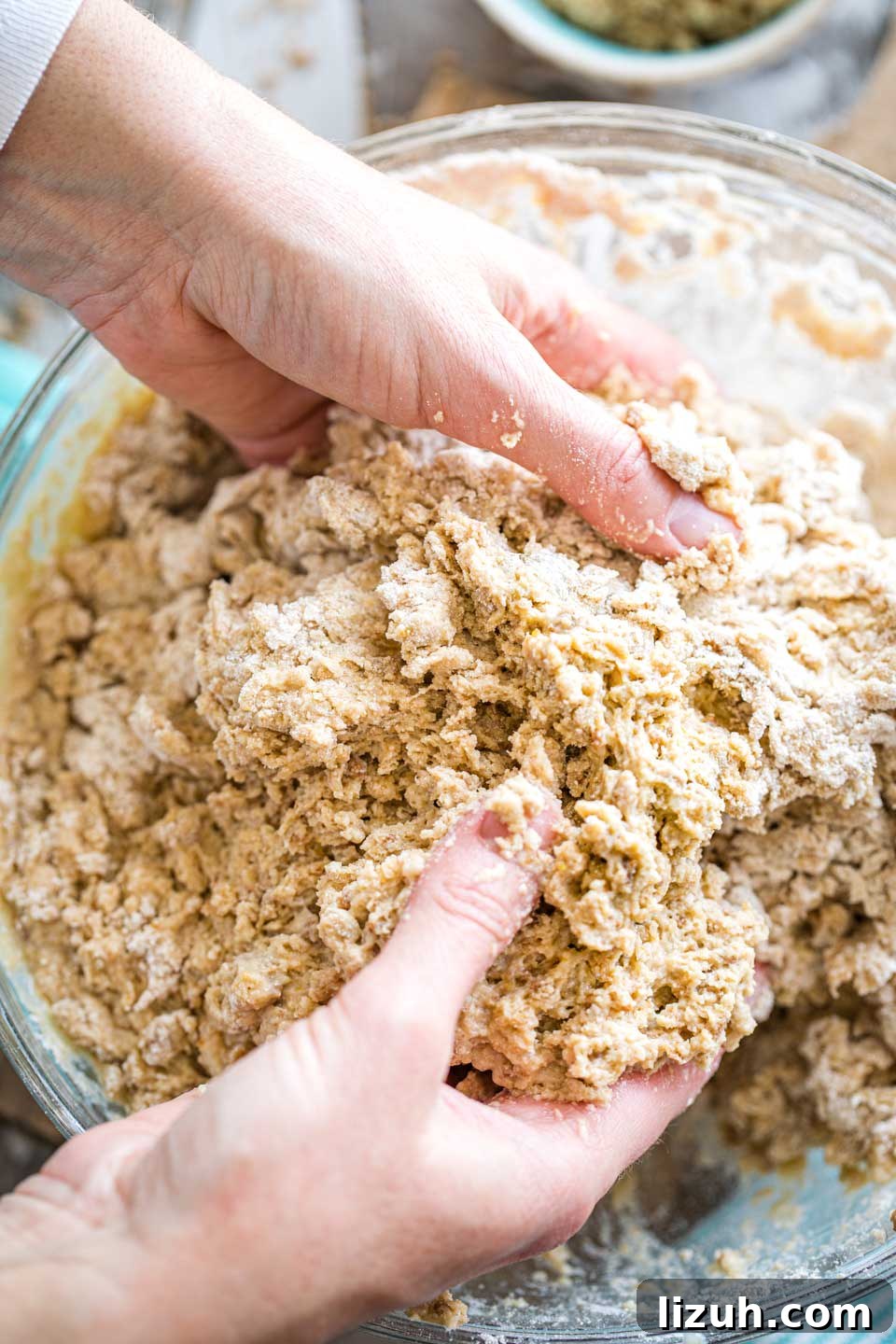 two hands plunged into bowl of homemade bread dough to mix it