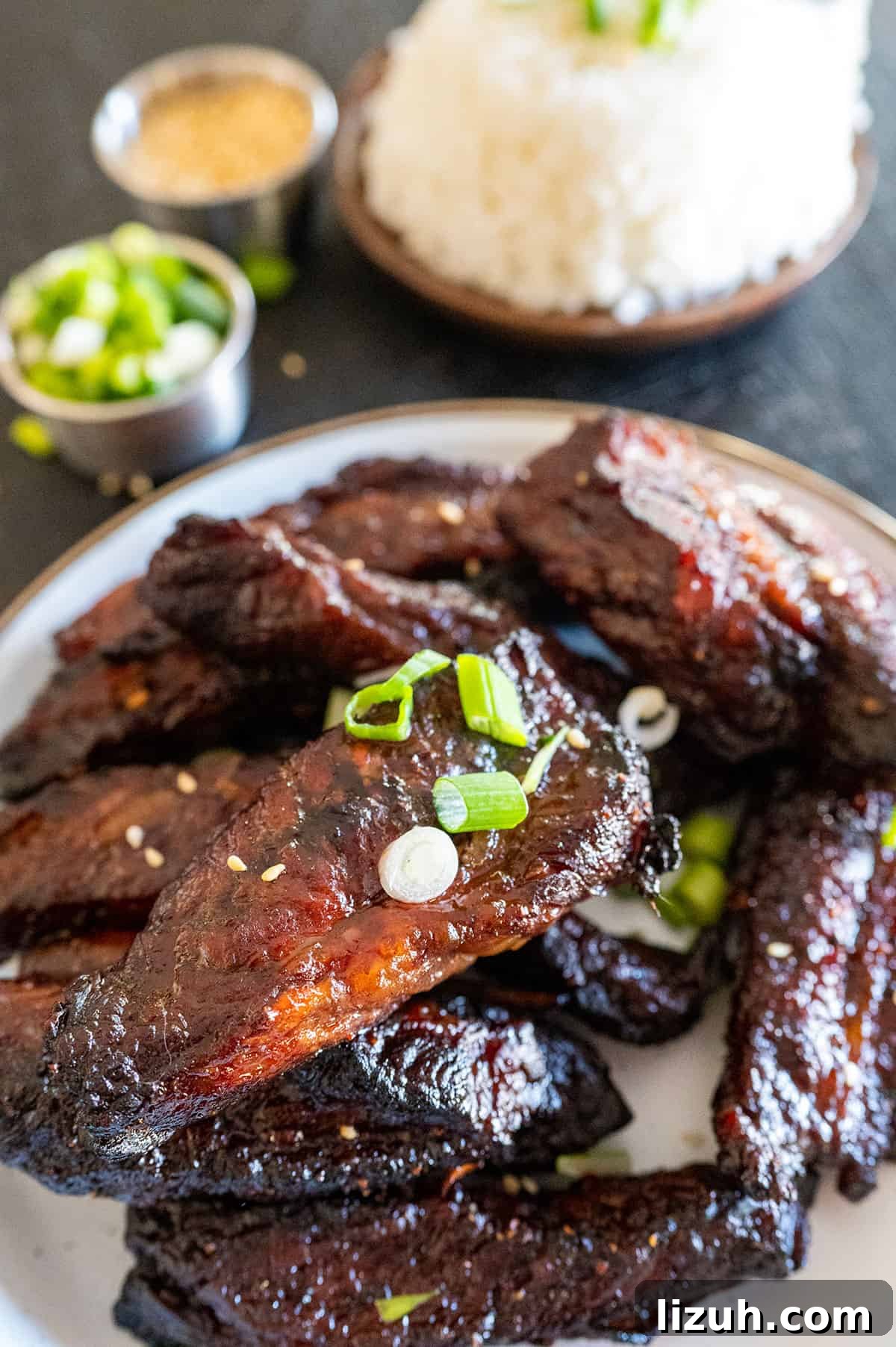 close up of teriyaki beef finger ribs on plate near bowl of rice.