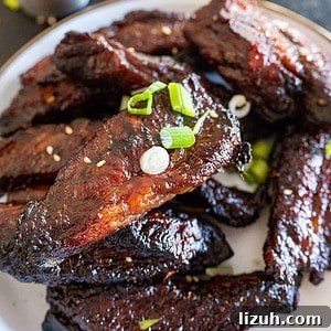 close up of teriyaki beef finger ribs on plate near bowl of rice.