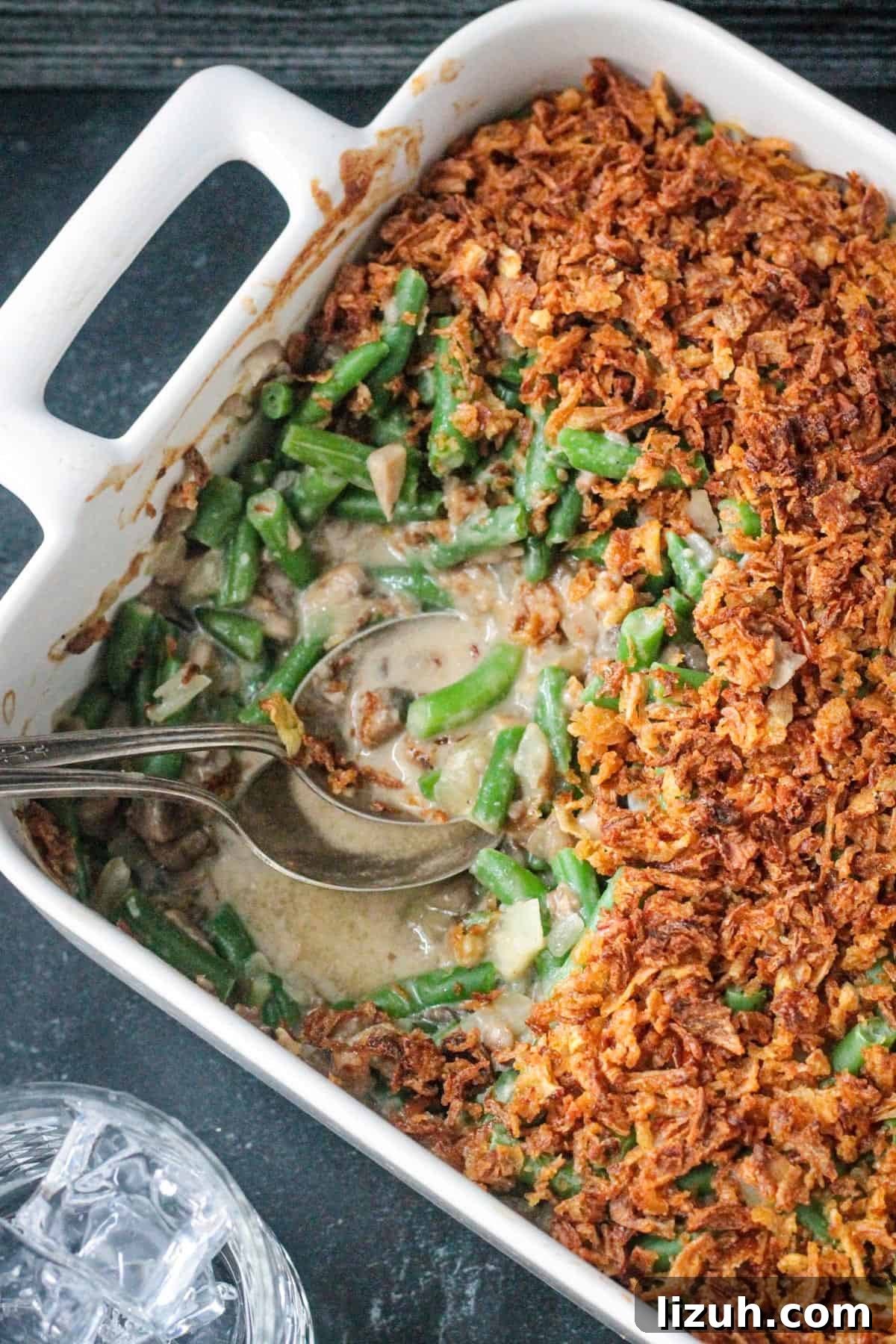 Two serving spoons in a pan of half eaten green bean casserole.
