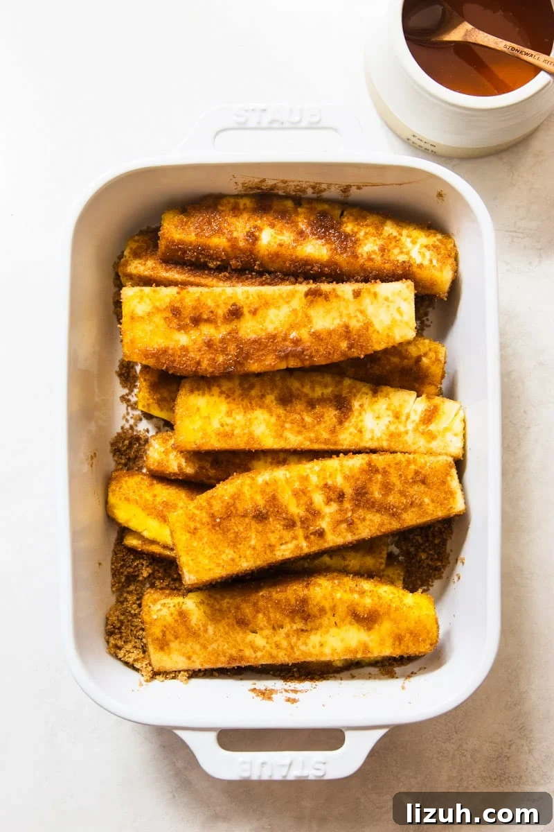 Brazilian-Style Grilled Pineapple Recipe for Sweet Tangy Dessert 5 Cinnamon and brown sugar coated pineapple in a white baking dish.