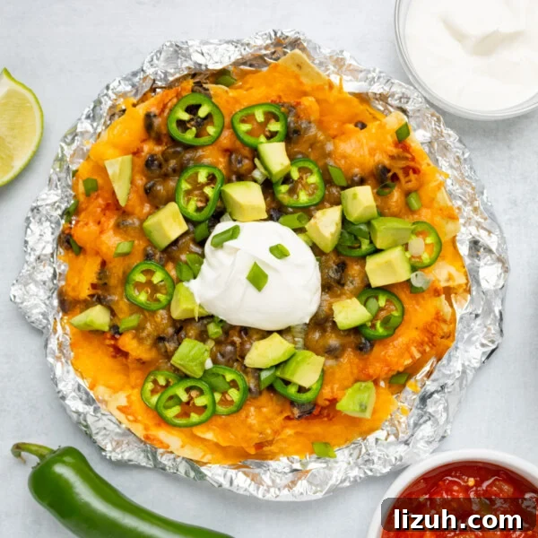 Loaded Tater Tot Nachos with Cheesy Beef and Jalapeños 12 An overhead image of air fryer nachos with toppings like sour cream, jalapenos, and sliced avocados.