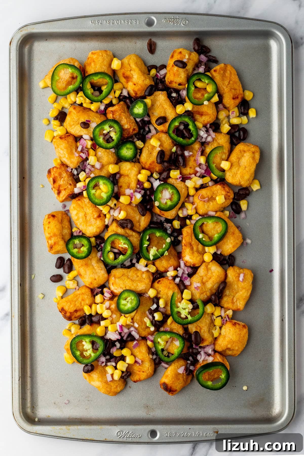 Loaded Tater Tot Nachos with Cheesy Beef and Jalapeños 6 An overhead image of adding the veggies and beans on the tater tots.
