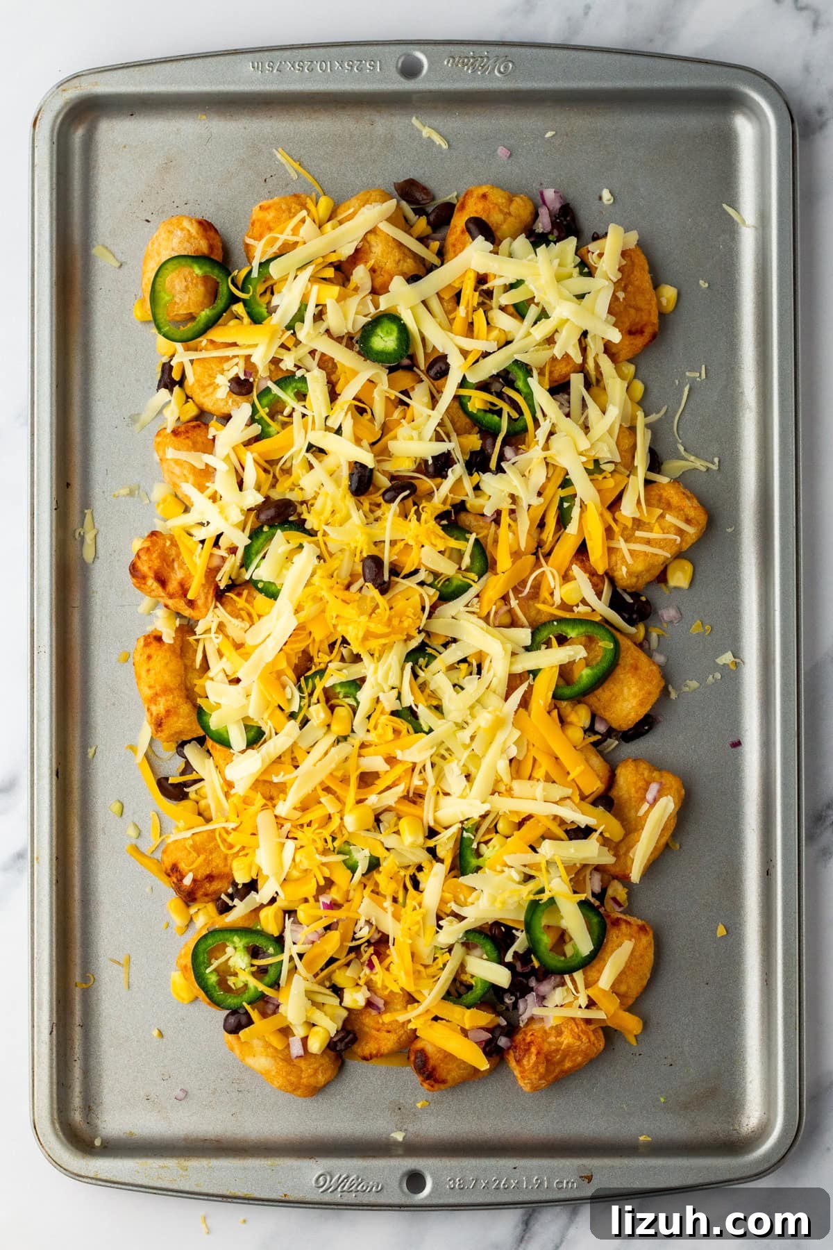 Loaded Tater Tot Nachos with Cheesy Beef and Jalapeños 7 An overhead image of sprinkling cheese on top.