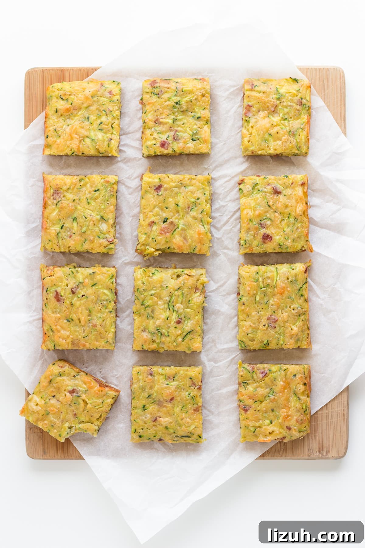 Savory Zucchini Slice Recipe with Cheesy Herb Crust 2 Square cut up pieces of zucchini slice on a wooden board lined with parchment paper.