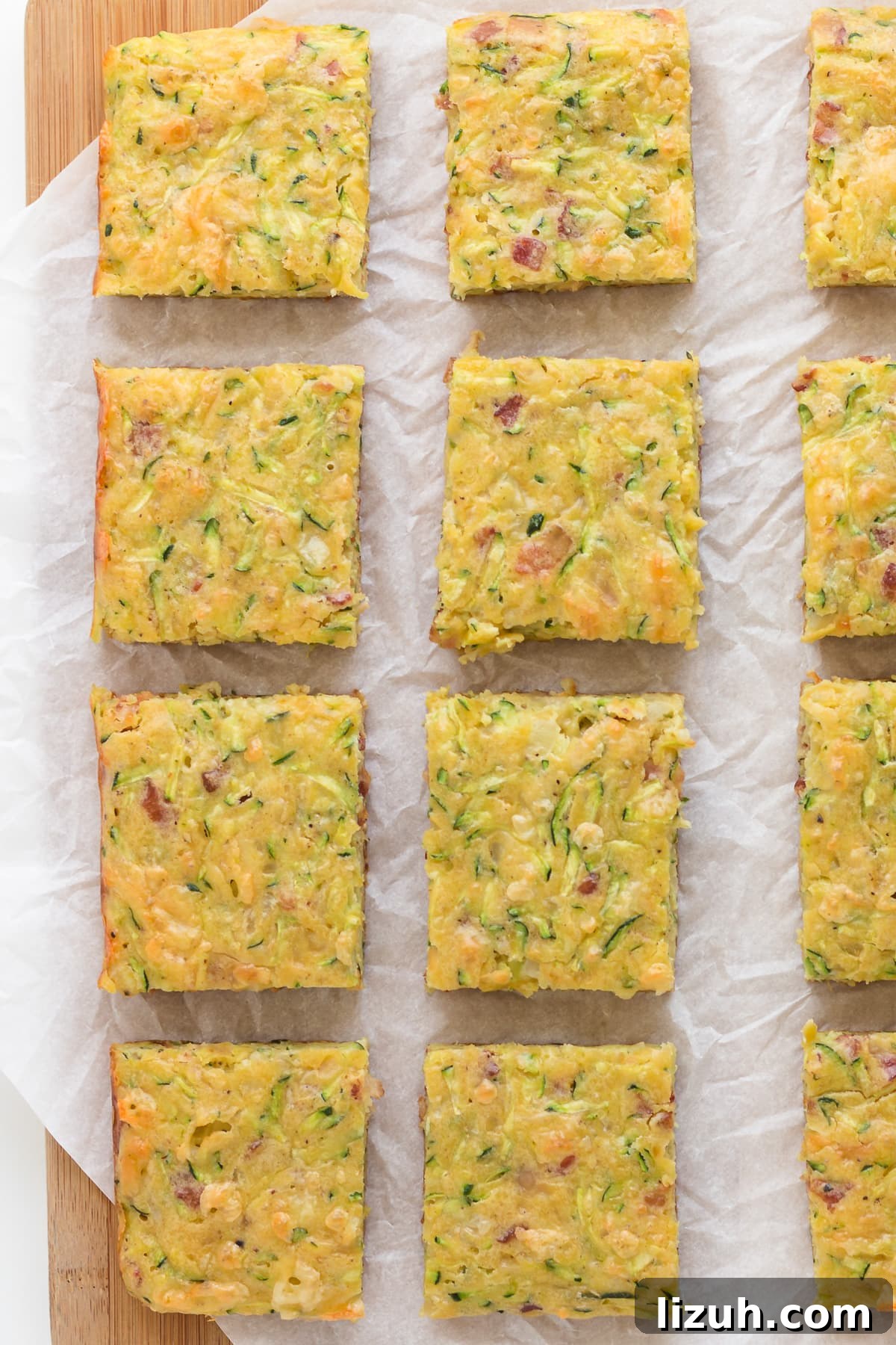 Savory Zucchini Slice Recipe with Cheesy Herb Crust 12 Closeup of square pieces of zucchini slice on a wood board lined with a piece of parchment paper.