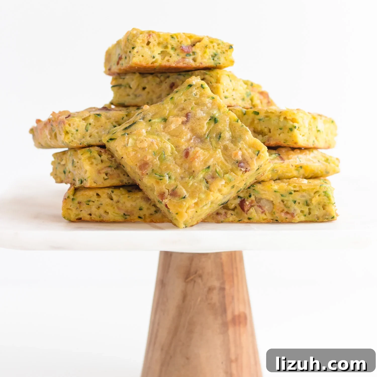 Savory Zucchini Slice Recipe with Cheesy Herb Crust 9 Pile of zucchini slice on a marble and wood cake stand.