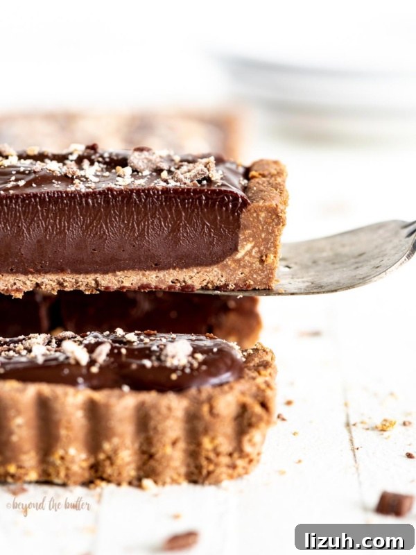Serving a slice of dark chocolate tart on white wood table.
