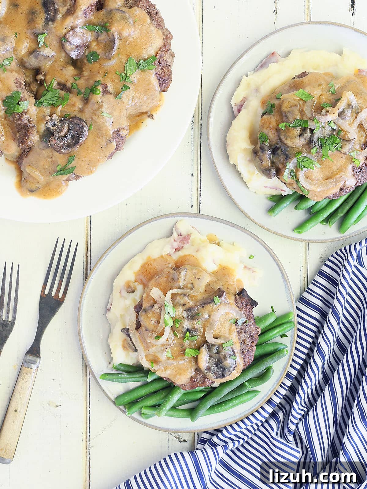 Back-to-School Dinner Ideas: Quick Family-Friendly Recipes 27 two white plates with hamburger steaks served over mashed potatoes and green beans with a serving plate of smothered hamburger steaks to the side