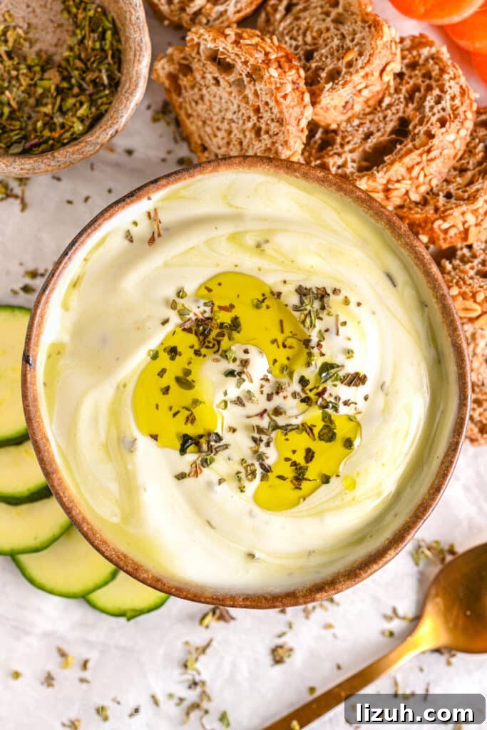 Creamy cottage cheese dip with a drizzle of olive oil and dried herbs, served with whole-grain bread, vegetables, and fresh zucchini slices.