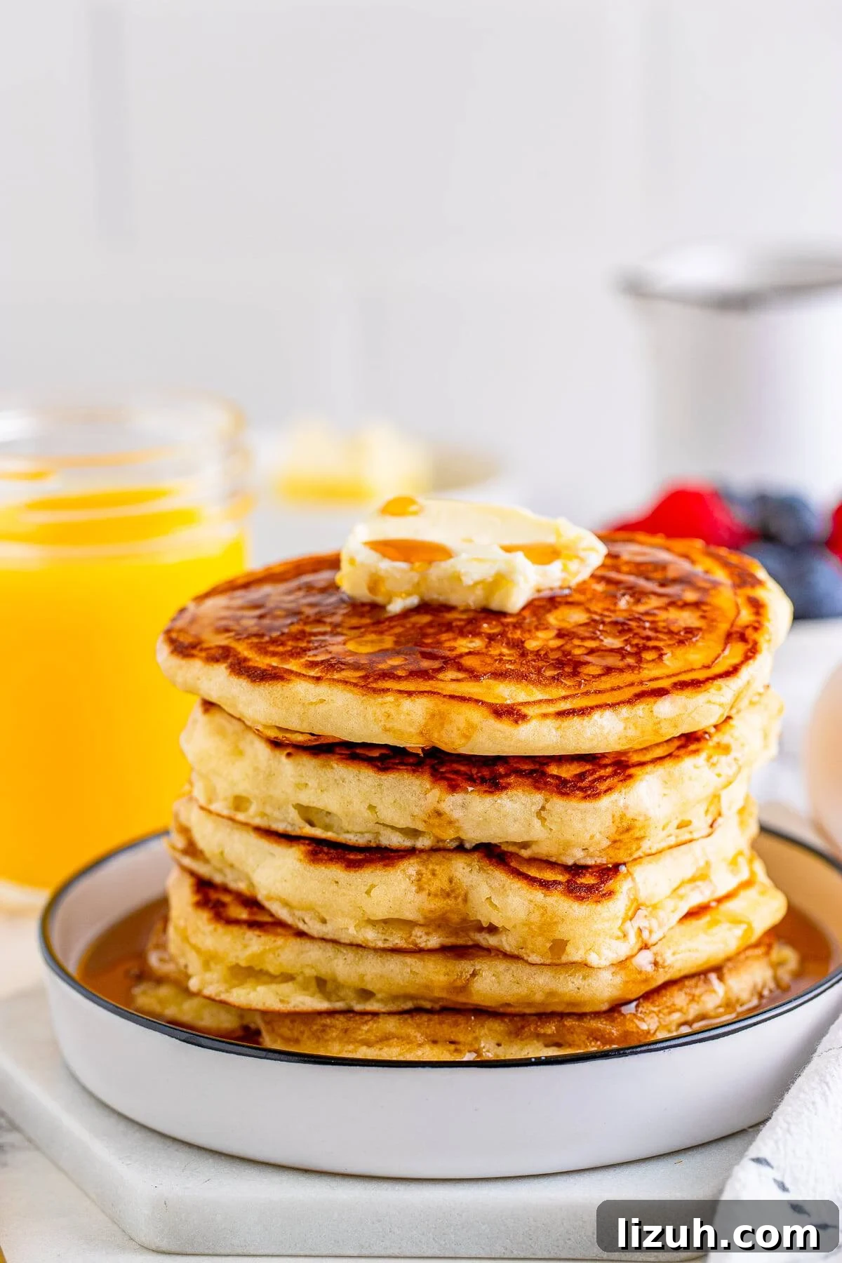 The Best Buttermilk Pancakes stacked on white plate with butter and syrup.