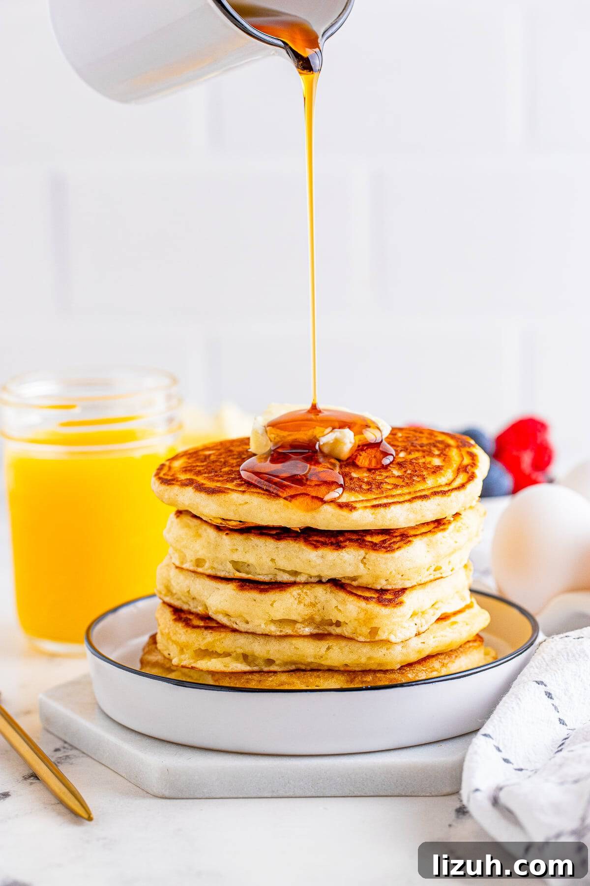 Syrup being poured over the stack of pancakes on white plate.